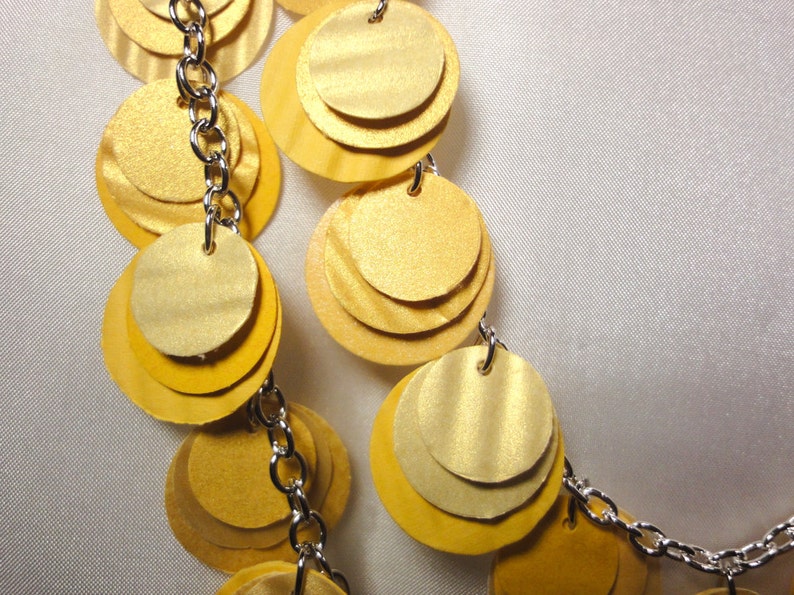May include: A gold necklace with multiple layers of round, overlapping discs connected by a silver chain.