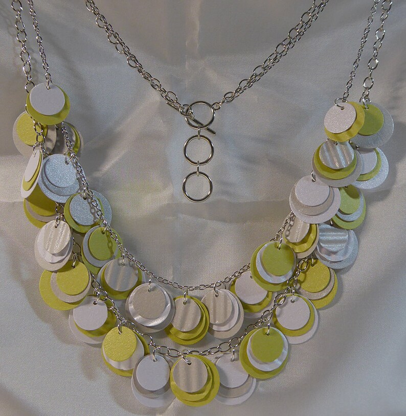 May include: A silver chain necklace with multiple layers of layered circles in shades of white and yellow.