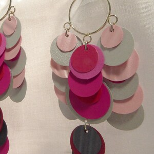 May include: A pair of dangle earrings with a silver hoop and multiple layers of pink, red, and gray circles.