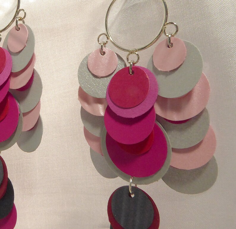 May include: A pair of dangle earrings with a silver hoop and multiple layers of pink, red, and gray circles.