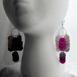 May include: A pair of dangle earrings with multiple layers of pink, gray, and black circles. The earrings are silver and have a hook closure.