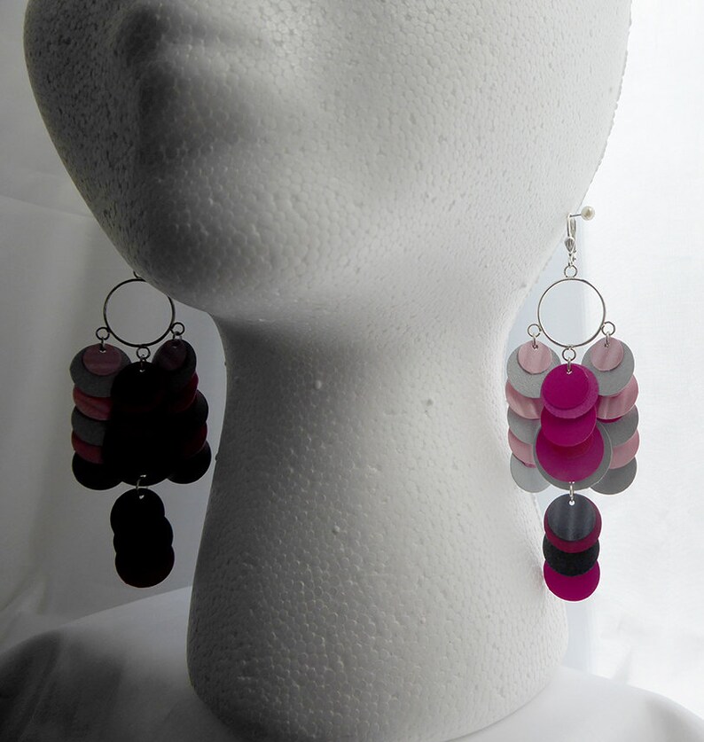 May include: A pair of dangle earrings with multiple layers of pink, gray, and black circles. The earrings are silver and have a hook closure.