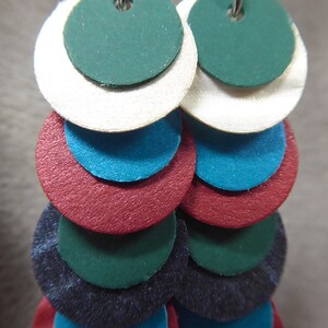 May include: A pair of dangle earrings with multiple layers of circles in shades of green, white, blue, red, and black.