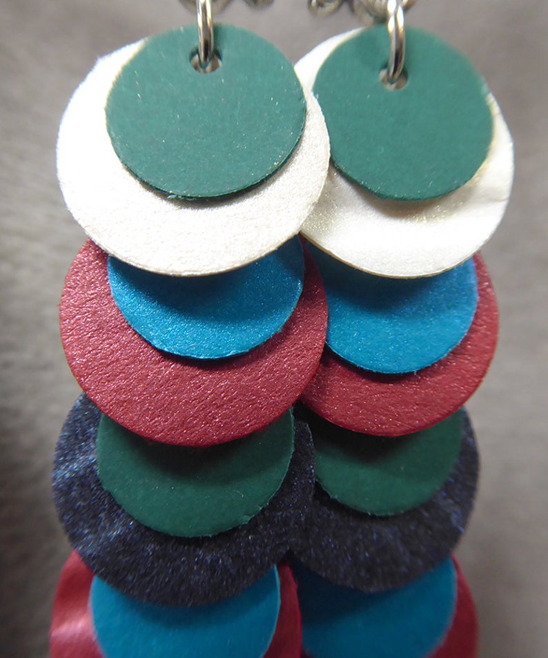 May include: A pair of dangle earrings with multiple layers of circles in shades of green, white, blue, red, and black.