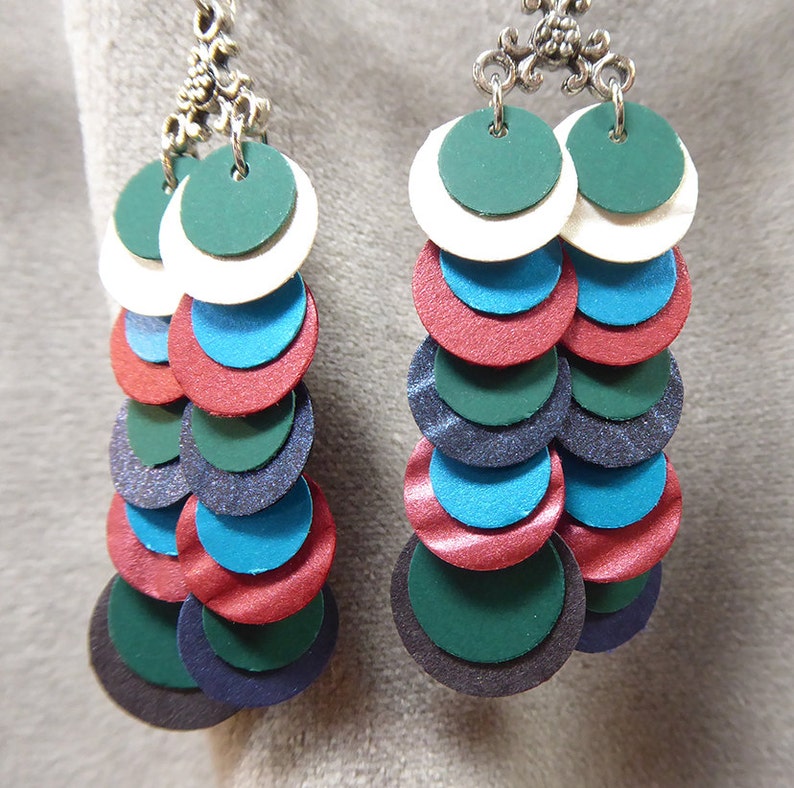 May include: A pair of dangle earrings with multiple layers of round discs in shades of green, blue, red, and white. The discs are layered in a graduated size, with the largest disc at the bottom. The earrings are attached to silver-toned hooks.
