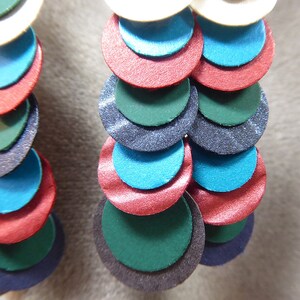 May include: A pair of earrings with multiple layers of colorful circles. The circles are in shades of teal, green, red, and black. The earrings are made of a shiny material.