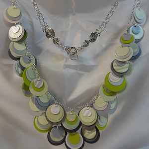 May include: A silver chain necklace with a silver clasp. The necklace is adorned with layered circles of green, gray, and white paper.