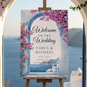 May include: A wedding welcome sign on a wooden easel. The sign features the words "Welcome to the Wedding" with the names Carla & Michael and the date 05/07/2026. Pink flowers and a blue arch frame the text.