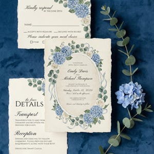 May include: Wedding invitation suite featuring watercolor blue hydrangeas and white roses. The suite includes an invitation, RSVP card, and details card, all with elegant calligraphy on textured paper. A sprig of eucalyptus and a blue hydrangea bloom are also present.