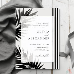 Op de afbeelding: Een zwart-witte huwelijksuitnodiging met een tropisch bladontwerp. De uitnodiging luidt "Kindly join us for the wedding of Olivia and Alexander" met de datum en tijd van de bruiloft, 20 augustus om 17:00 uur, en het adres, 123 Anywhere St., Any City, ST 12345. De uitnodiging bevat ook de tekst "reception to follow".