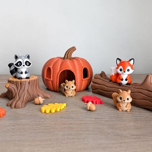 May include: A set of small plastic animal figurines including a raccoon, a fox, and two squirrels, accompanied by a hollow orange pumpkin, a brown tree stump, a brown log, and several small colorful leaf and acorn shaped accessories.