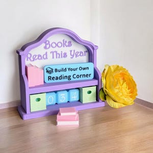 Könnte beinhalten: Ein lila Bücherregal mit dem Text "Books Read This Year" und "Build Your Own Reading Corner". Es hat ein Regal mit den Blöcken 034 und einen Stapel Miniatur-Rosa Bücher. Rechts ist eine große gelbe Rose.