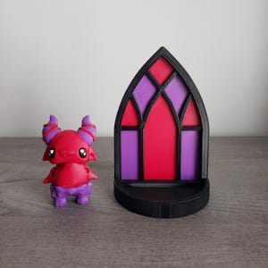 May include: A red and purple 3D printed figurine of a cartoon devil with horns and a stained glass window archway.