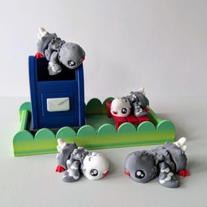 May include: Three gray and white bird figurines with red accents. One bird is perched on top of a blue mailbox, another is sitting on a red bench, and the third is lying on the ground. The figurines are on a green and white platform.