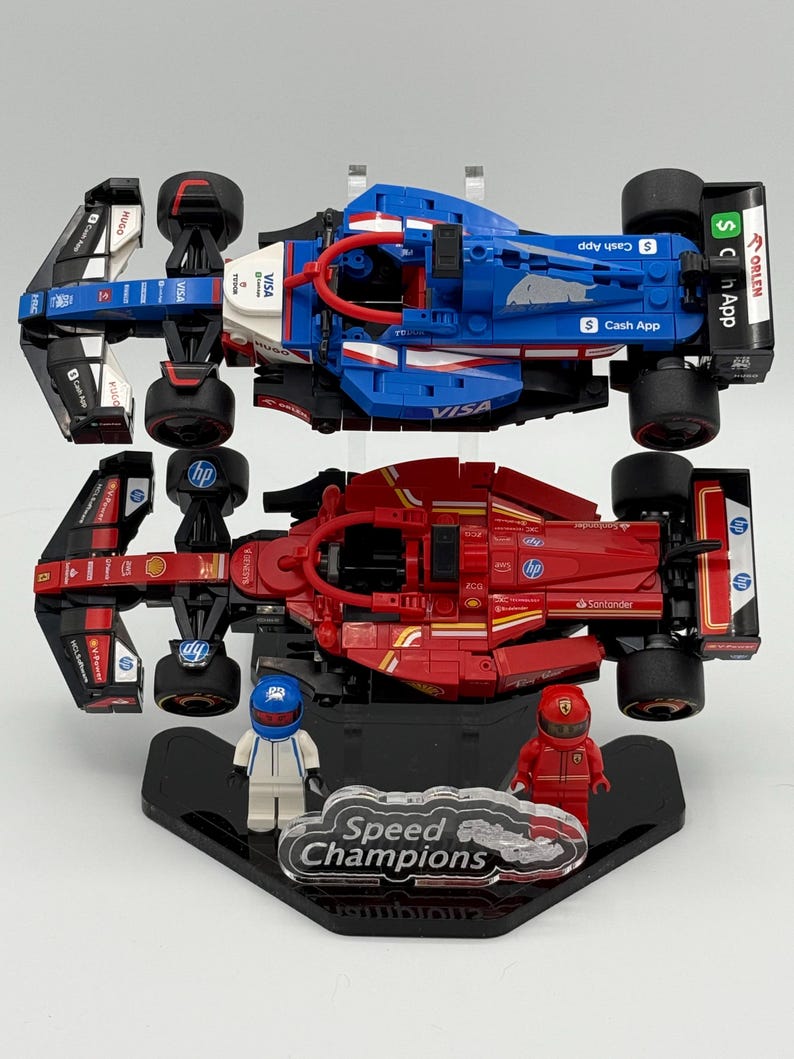 May include: Two Lego Speed Champions race cars on display stands. The top car is blue, white, and red with the logos "VISA", "Cash App", and "ORLEN". The bottom car is red with the logos "Santander", "HP", and "Shell".