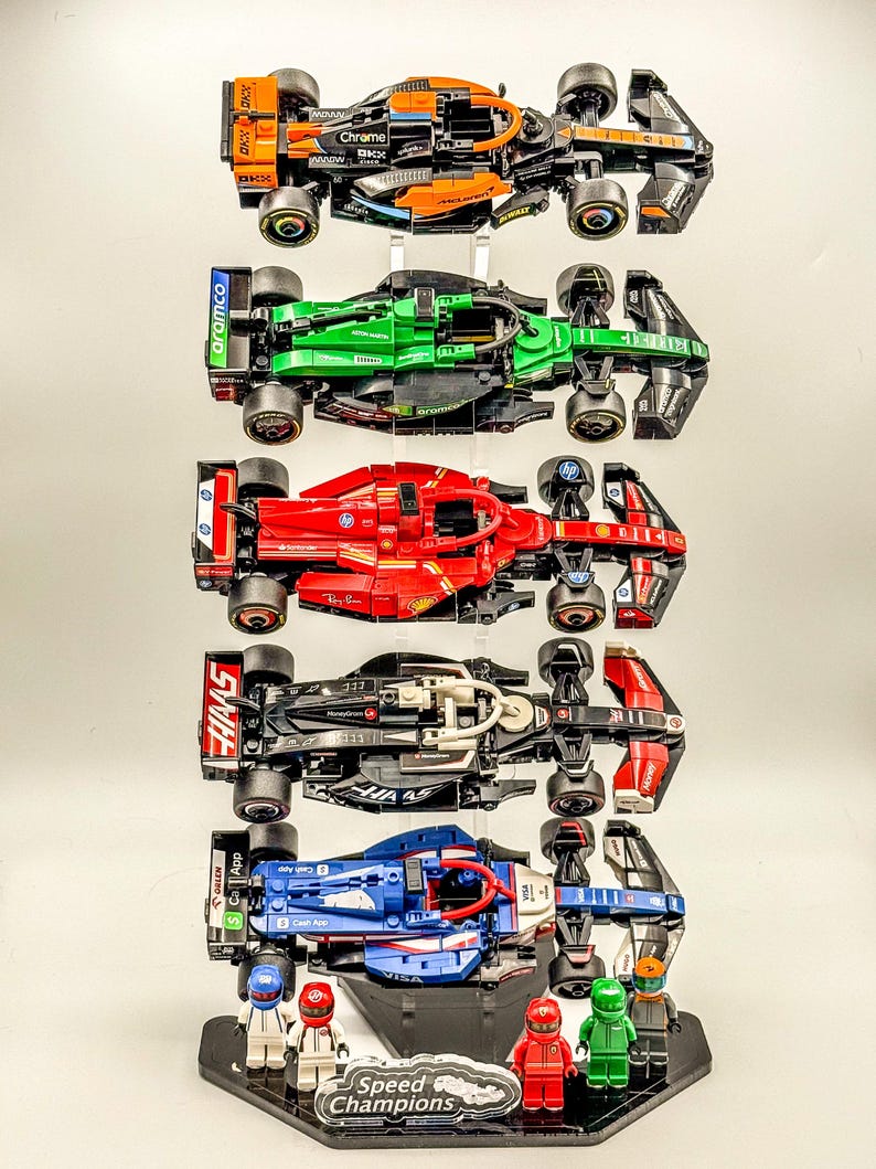 May include: A display stand with five miniature Lego Formula 1 race cars. The cars are in different colors and have different sponsors, including Aramco, Haas, and Chrome. The stand is black with a silver base and the words "Speed Champions" printed on it.