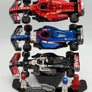 May include: Three Lego Speed Champions race cars on a black display stand. The cars are a red Ferrari, a blue and white car, and a black and red car. Each car has a driver figure next to it.