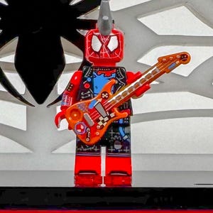 May include: A red and black Lego figure with a mohawk and a guitar. The figure is wearing a black vest, blue shirt, and black shorts. The guitar is orange and brown with a checkered design.