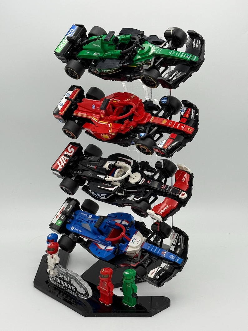 May include: A display stand with four Lego Speed Champions race cars. The cars are stacked on top of each other and are in different colors, including green, red, black, and blue. The stand is made of clear acrylic and has a black base with the words "Speed Champions" printed on it.