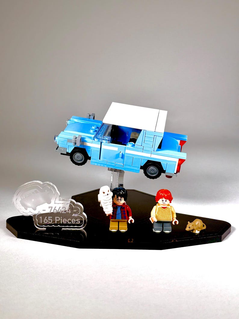 May include: A Lego set featuring a light blue car with a white roof, and three mini-figures. The set includes a white owl, a boy with black hair, and a boy with red hair. A brown rat is also included. The set is displayed on a black stand.