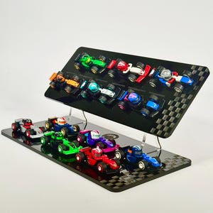 May include: A display stand holding multiple miniature race cars. The cars are various colors, including red, green, blue, and orange. The stand is black with a checkered pattern on the edges.