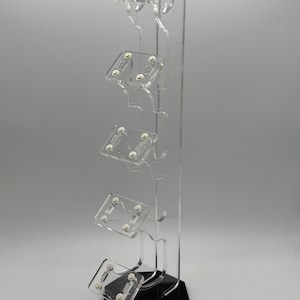 May include: A clear acrylic stand with five slots for holding video game controllers. The stand has a black hexagonal base.