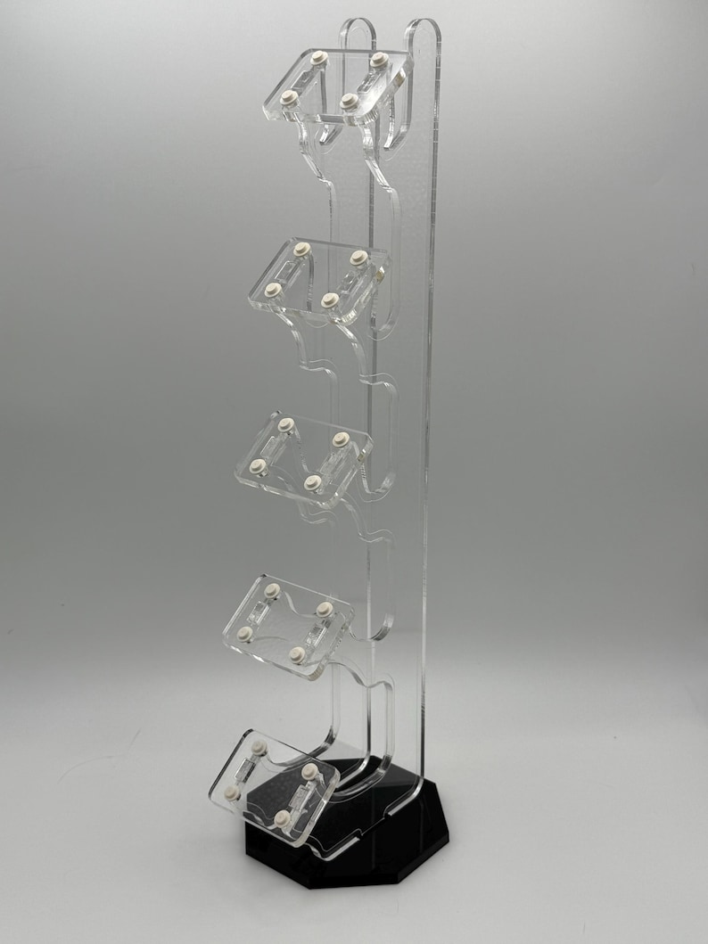 May include: A clear acrylic stand with five slots for holding video game controllers. The stand has a black hexagonal base.