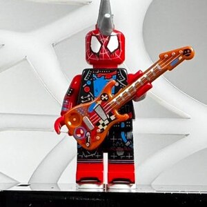May include: A red and black Lego Spider-Man figure with a silver mohawk and a guitar. The guitar is orange and decorated with various designs. The figure is standing on a black surface with a white web design in the background.