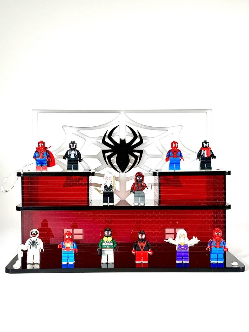 May include: A display featuring various Spider-Man-themed Lego minifigures. The display has a red brick facade and a white spiderweb design with a black spider emblem. The minifigures are in various colors and costumes.