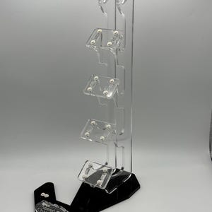 May include: A clear acrylic display stand with five slots for holding small cars. The stand has a black base with the words "Speed Champions" printed on it.