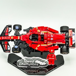 May include: A red Lego Ferrari Formula 1 race car with black wheels and a black and red driver figure. The car is on a black display stand with a clear plastic plaque that says "Speed Champions".