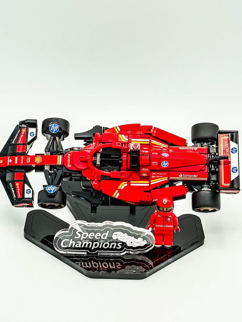 May include: A red Lego Ferrari Formula 1 race car with black wheels and a black and red driver figure. The car is on a black display stand with a clear plastic plaque that says "Speed Champions".