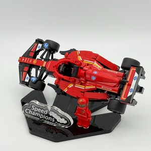 May include: A red Lego Speed Champions Ferrari Formula 1 race car with a black and white driver figure on a black display stand. The car has the logos of Santander, HP, and Shell on the side.