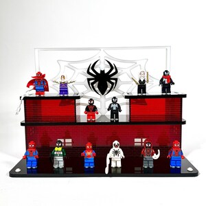 May include: A display stand featuring various Spider-Man themed minifigures. The stand has a red brick design with a black spider emblem and web background. The minifigures are in various poses and costumes.