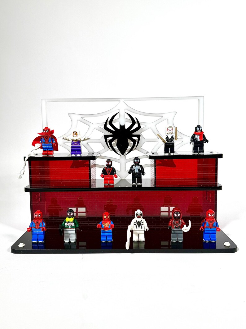 May include: A display stand featuring various Spider-Man themed minifigures. The stand has a red brick design with a black spider emblem and web background. The minifigures are in various poses and costumes.