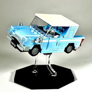 May include: A light blue Lego car model with a white roof, displayed on a clear stand with a black hexagonal base. The car has black tires and the license plate reads "7990 TD".