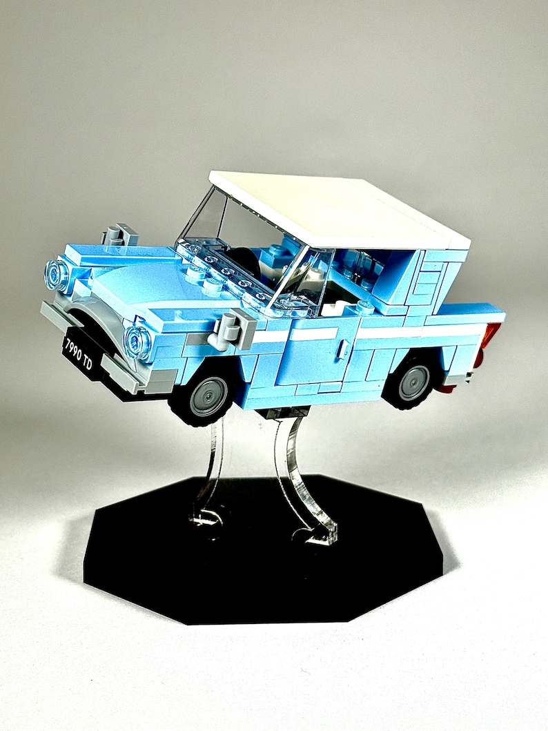 May include: A light blue Lego car model with a white roof, displayed on a clear stand with a black hexagonal base. The car has black tires and the license plate reads "7990 TD".