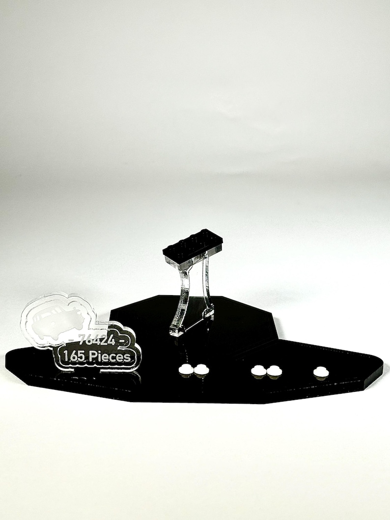 May include: A black display stand with a clear support structure holding a black rectangular object. The stand has a unique shape and includes the text "76424 - 165 Pieces" on a white cloud-shaped element. Several small white cloud-shaped elements are also present.