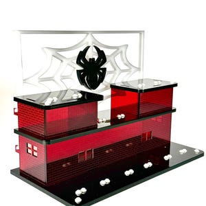 May include: A red and black decorative building with a spider web and spider design. The building has a brick pattern, windows, and a black base. The spider web is white, and the spider is black.