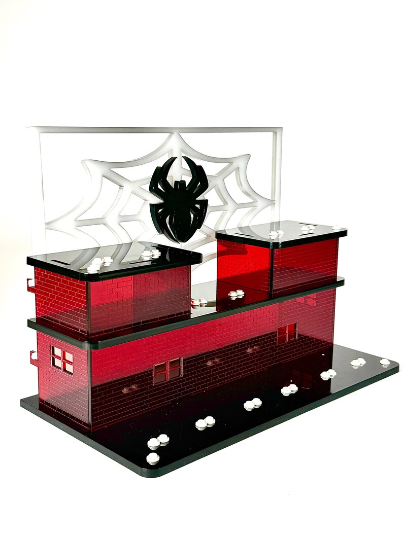 May include: A red and black decorative building with a spider web and spider design. The building has a brick pattern, windows, and a black base. The spider web is white, and the spider is black.