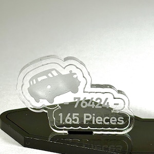 May include: A clear acrylic car-shaped ornament with the number "76424" and the text "1.65 Pieces" etched into it. The ornament sits on a black base and is set against a light gray background.