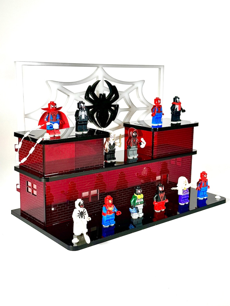May include: A display featuring multiple Spider-Man action figures on a two-tiered red brick-style platform. A white spiderweb and a black spider silhouette are in the background. The figures are in various costumes.