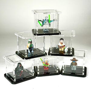 Op de afbeelding: Verzameling van zes transparante acryl vitrinekasten, elk met een Star Wars Lego-figuur. De figuren omvatten Darth Maul, Ahsoka Tano en een Mandalorian. Elke kast heeft een zwarte basis.