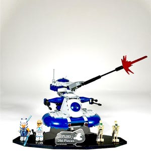 May include: A blue and white Lego set featuring a vehicle with a long, black and red weapon. The set includes several mini-figures, including two battle droids and two other characters. The set is on a black base and includes the text "75283 - 286 Pieces."
