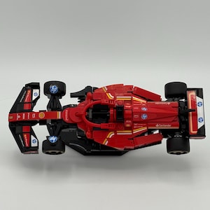 May include: A red and black Lego Formula 1 race car with the logos of Santander, Shell, and HP. The car is on a white surface.