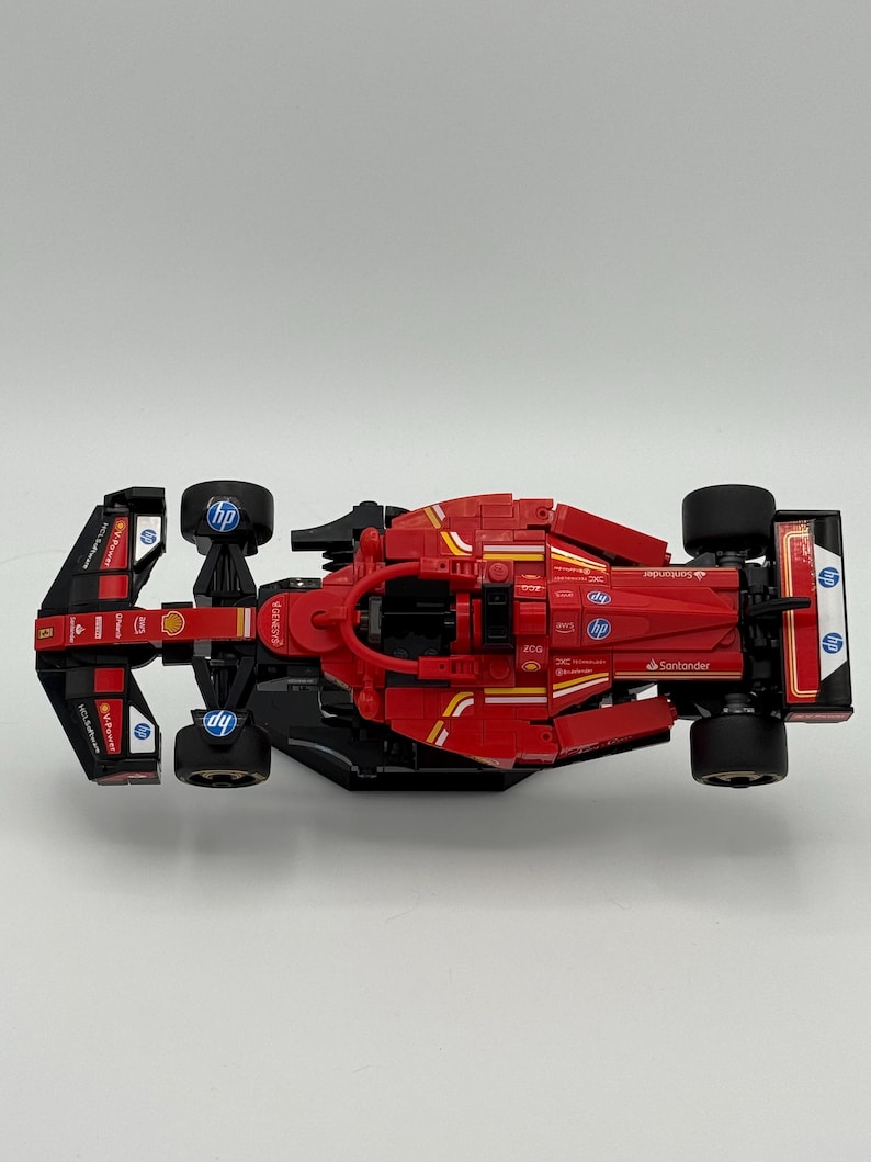 May include: A red and black Lego Formula 1 race car with the logos of Santander, Shell, and HP. The car is on a white surface.