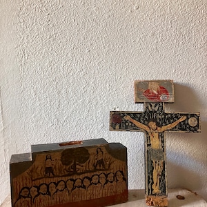 May include: Two hand-painted wooden religious items. One is a cross with a figure of Jesus, the other is a rectangular block with a painted scene of figures. Both items have a rustic, aged appearance.