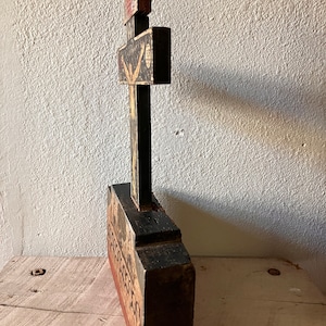 May include: A tall, wooden religious artifact with a cross design. The piece is painted black, red, and beige, with detailed illustrations. The cross is mounted on a rectangular base, and the overall style suggests a vintage or antique aesthetic.