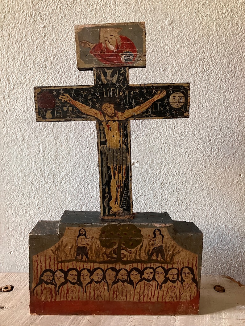 May include: Hand-painted wooden cross with a detailed depiction of Jesus on the cross, surrounded by stars and figures. The base features additional painted scenes with figures and flames. The cross is mounted on a rectangular base.