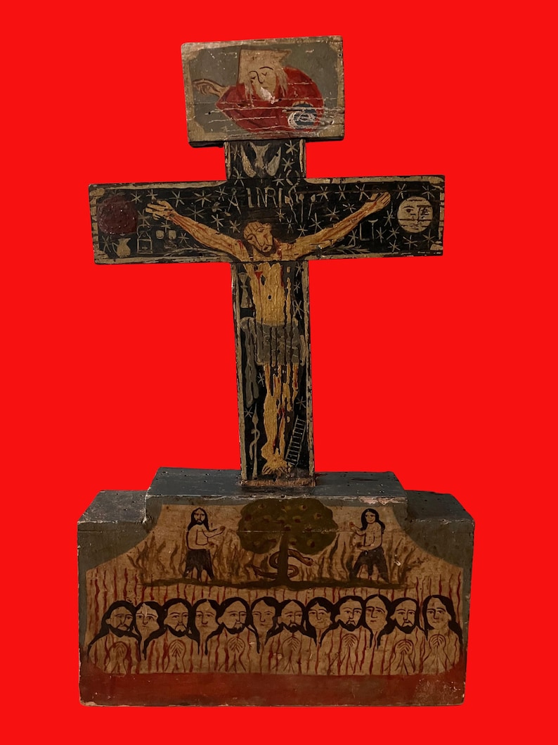May include: A hand-painted wooden crucifix with a red background. The cross features a depiction of Jesus Christ, with additional painted figures and symbols. The base of the cross has a painted scene with multiple figures. The artwork is done in a folk art style.